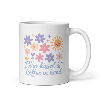 White ceramic mug with pastel flowers, smiling sun, and “Sun-kissed & Coffee in Hand” text – summer coffee mug for moms by Happily Styled